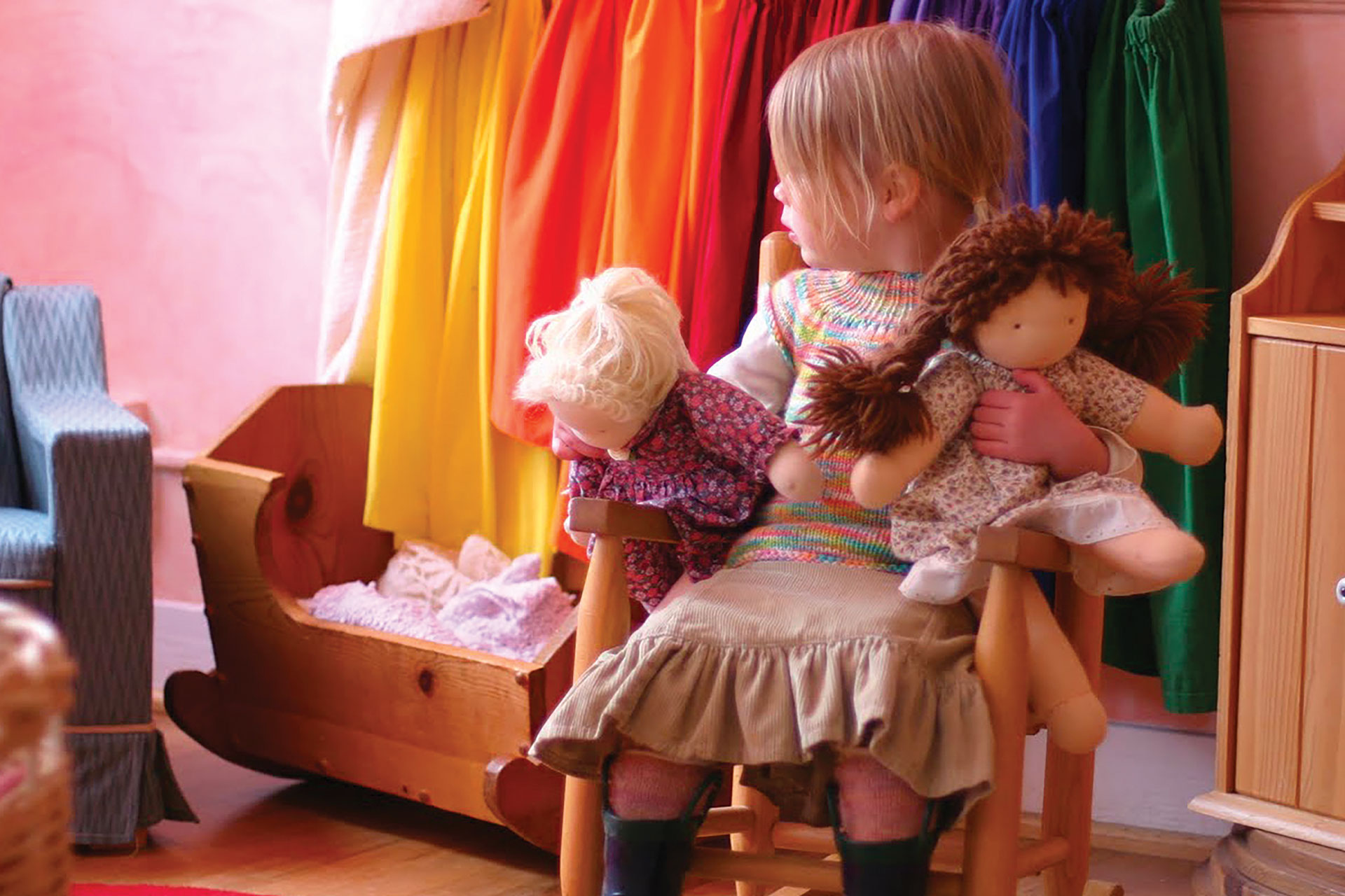 Bambina che gioca con bambole di stoffa in un’aula della scuola Waldorf, circondata da materiali naturali e colori caldi